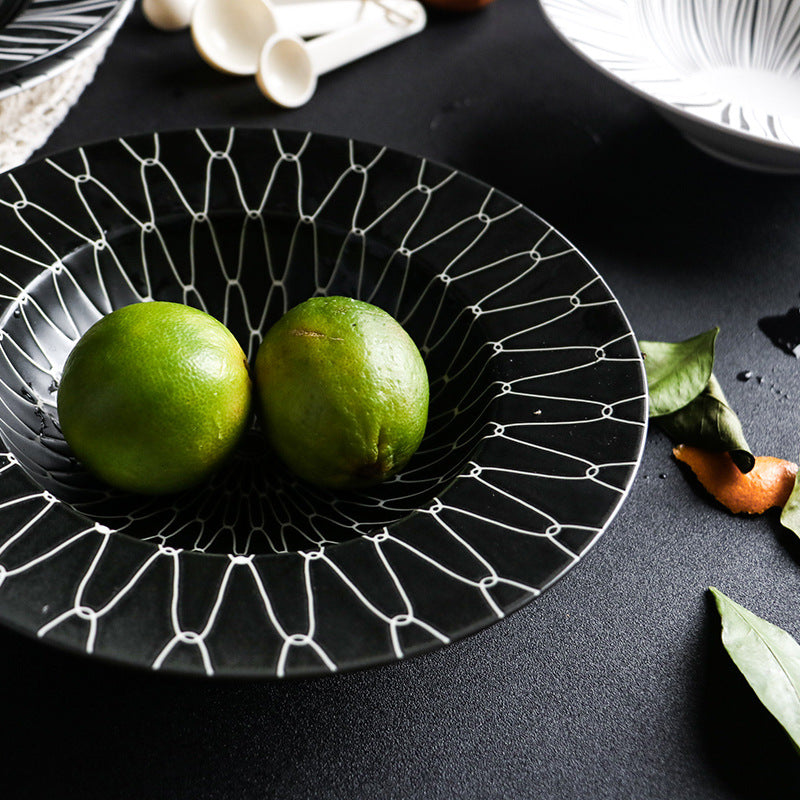 Black decorative plate with white lines holding two green fruits on a dark surface.