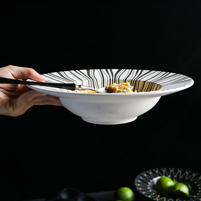 Hand holding a white bowl with black stripes filled with food on a dark background