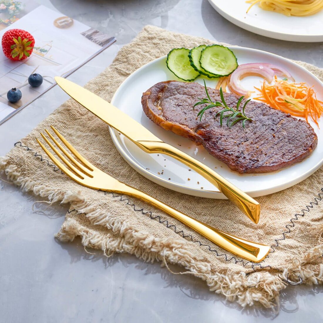 Plated dish with meat, vegetables, and gold cutlery on a textured surface.