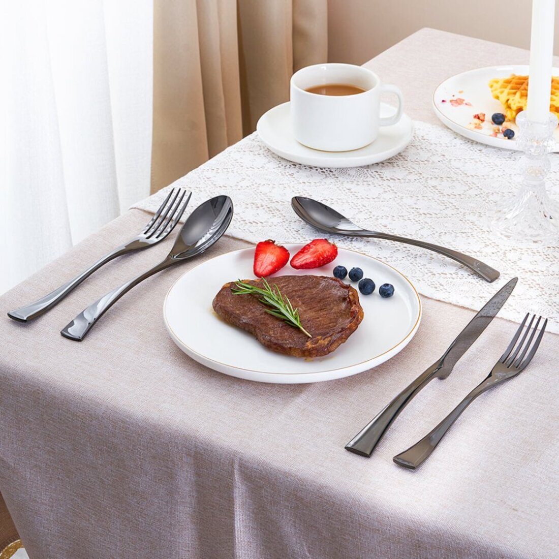 Dinner setting with steak, fruit, and cutlery on a tablecloth.