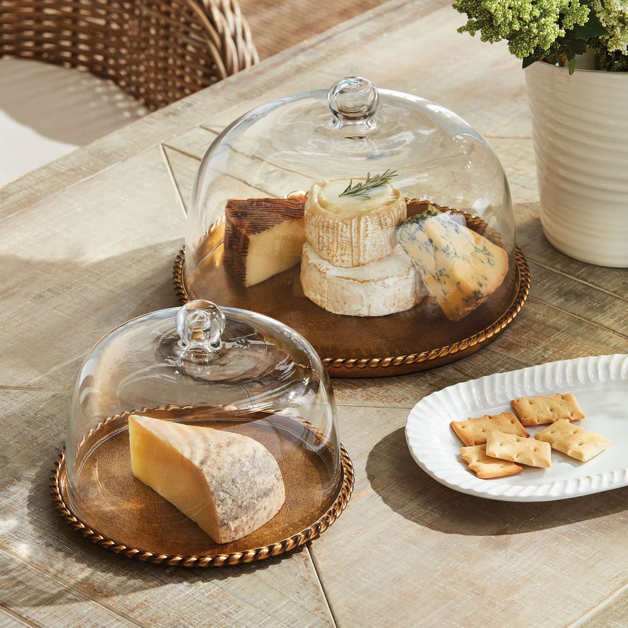 Glass dome covers displaying various types of cheese on a wooden tray with crackers on a table.