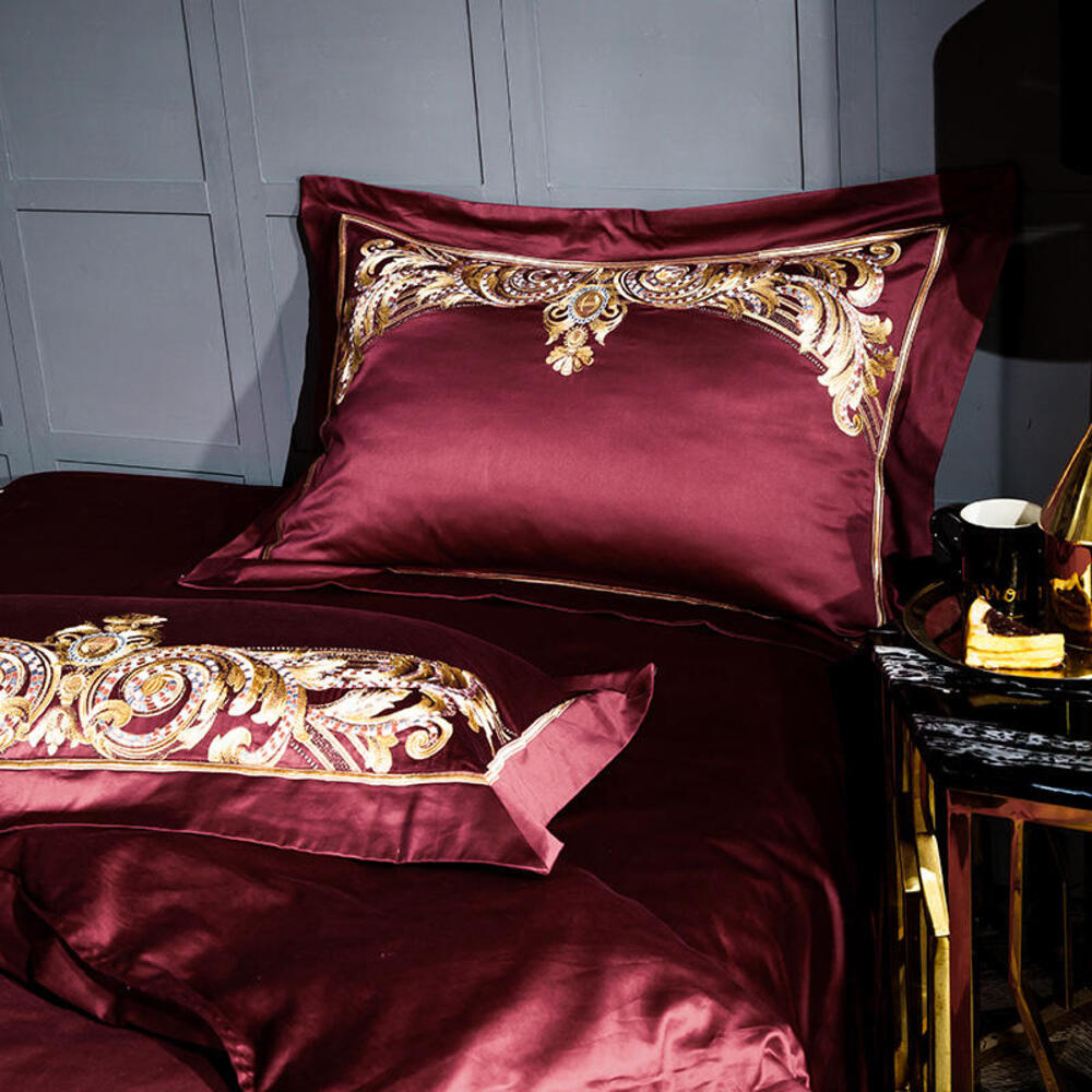 Burgundy satin bedding set with gold embroidery on a bed against a gray paneled wall.