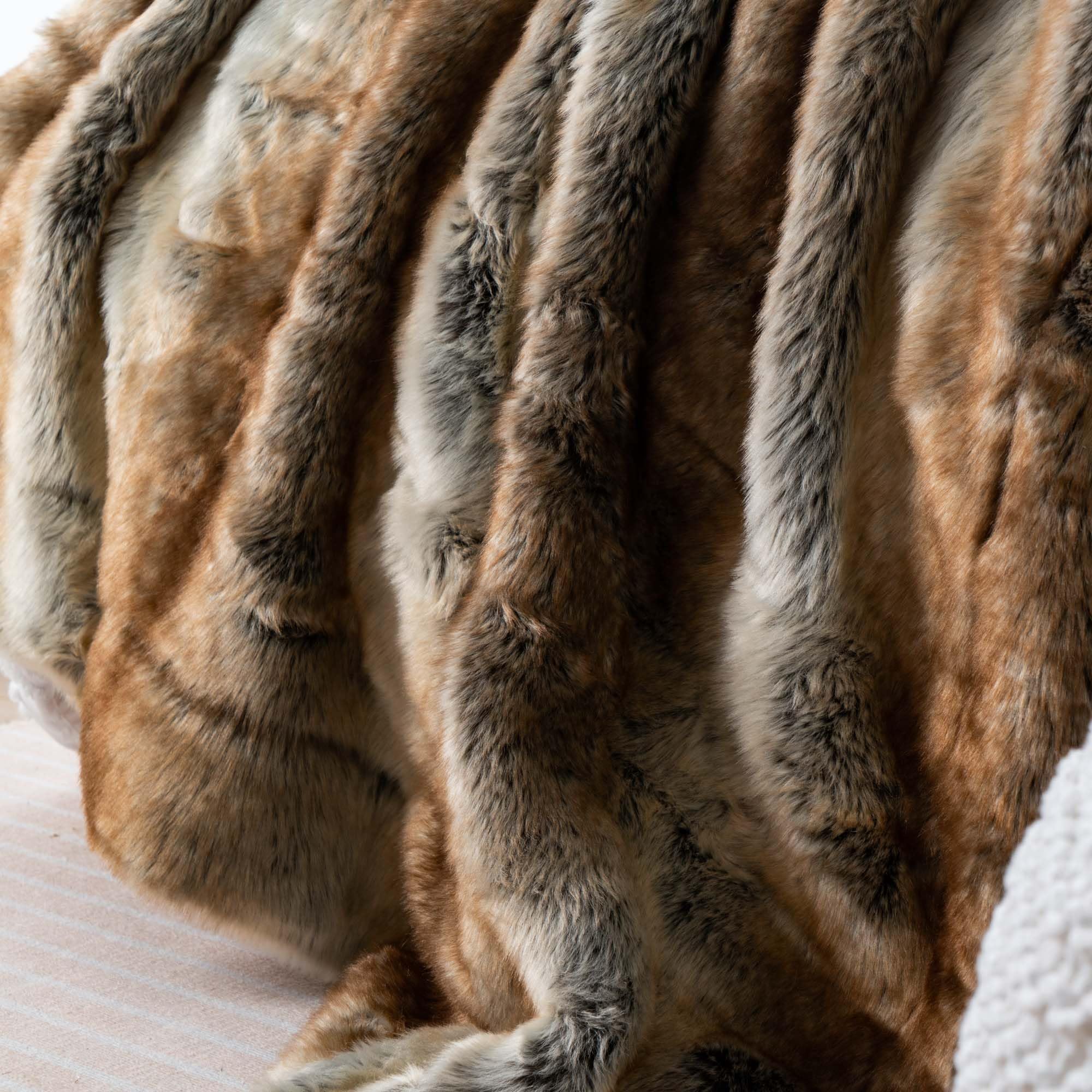 Close-up of a fur blanket with brown and gray tones on a soft surface.