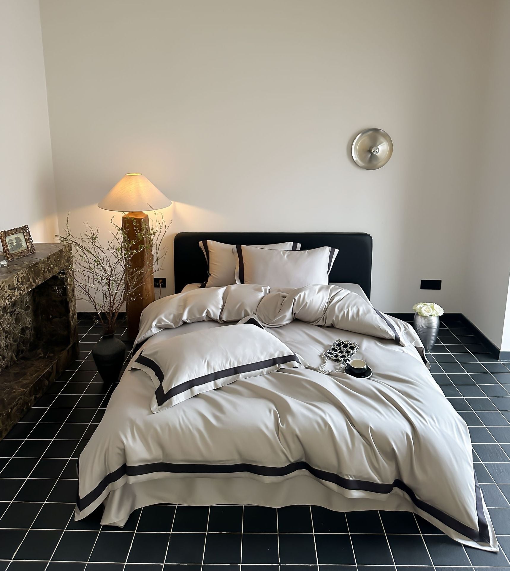 Neatly made bed with white bedding and black trim in a bedroom setting.