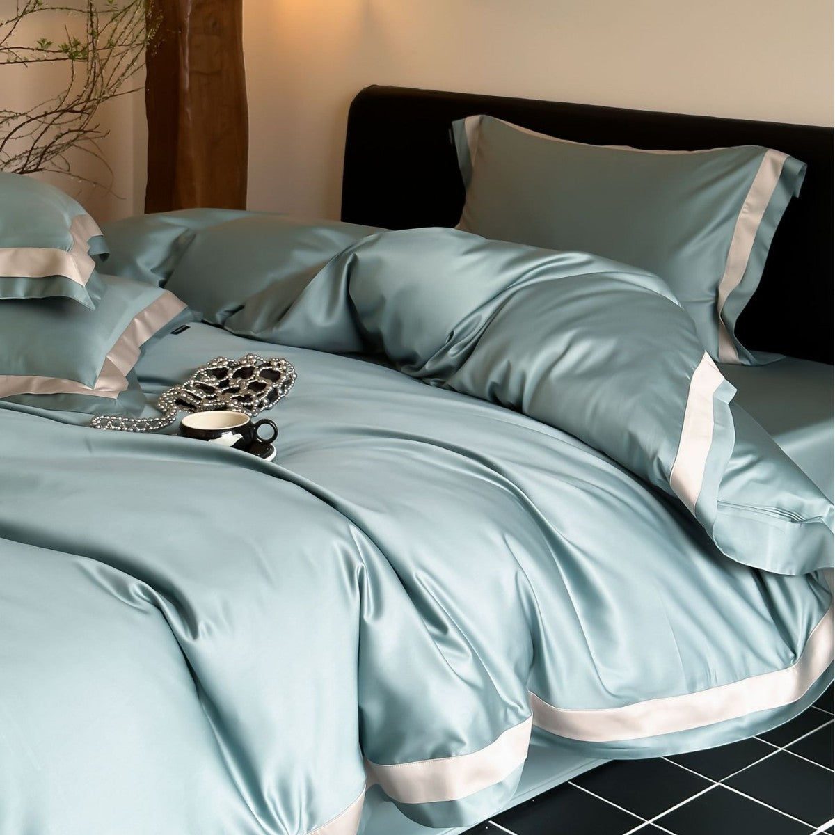 Teal satin bedding set with decorative pillows on a bed.