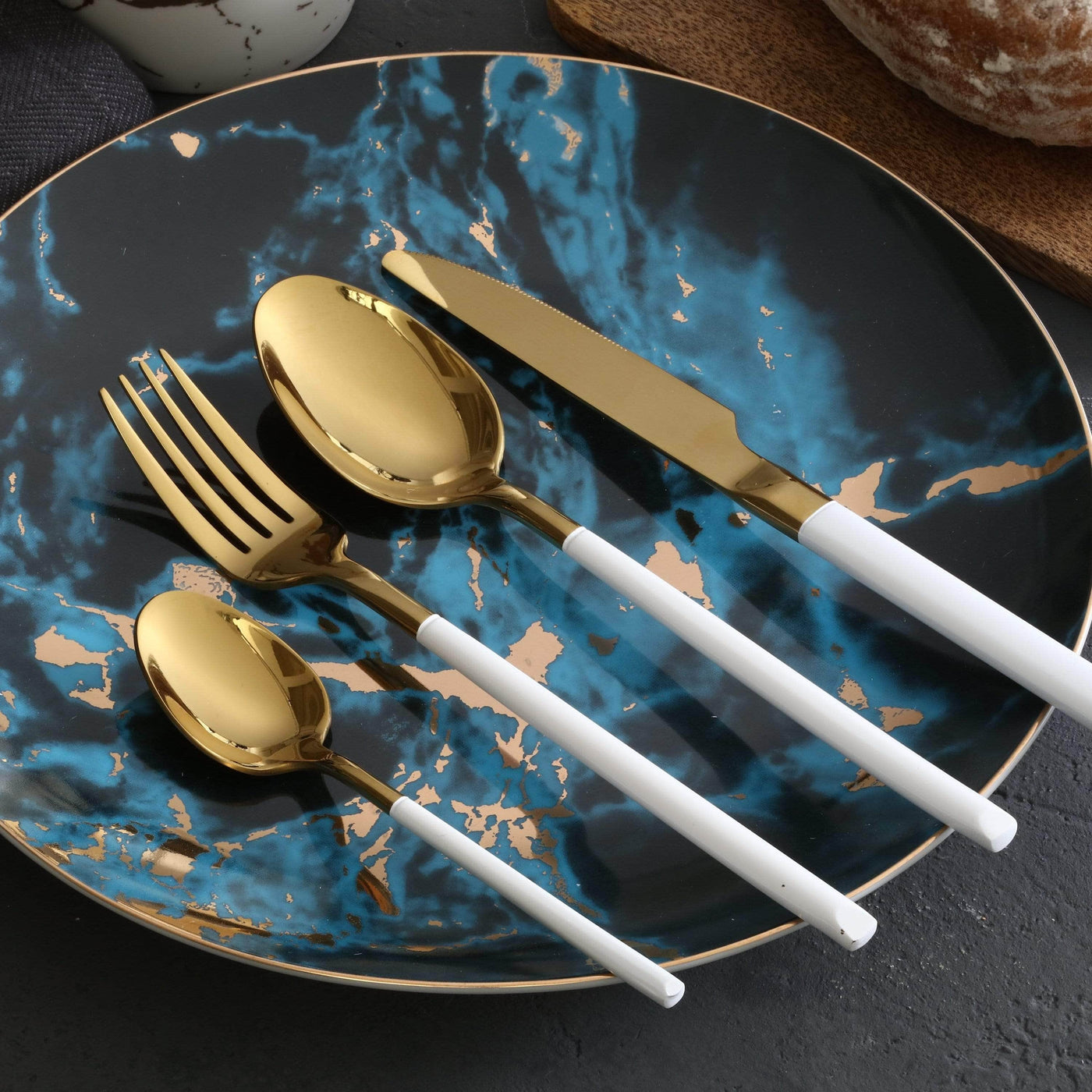 Gold cutlery set with white handles on a blue marbled plate.