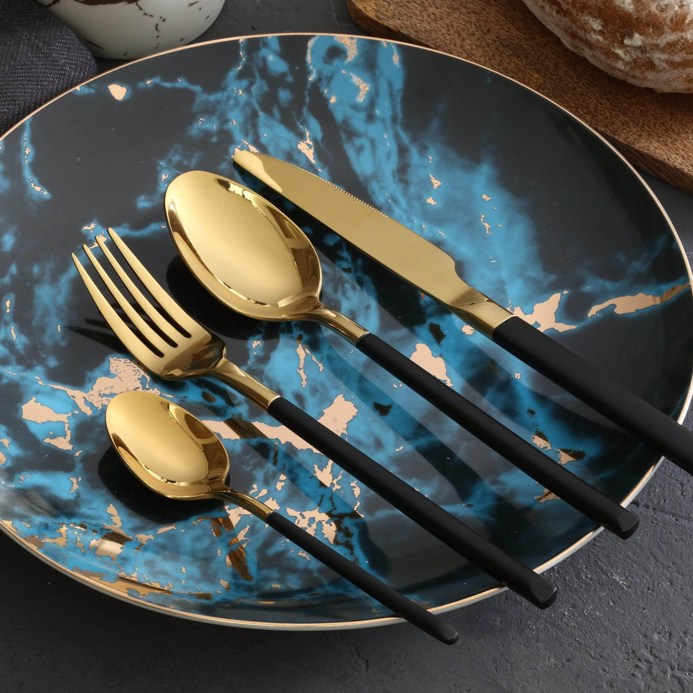 Gold cutlery set with black handles on a blue marbled plate.