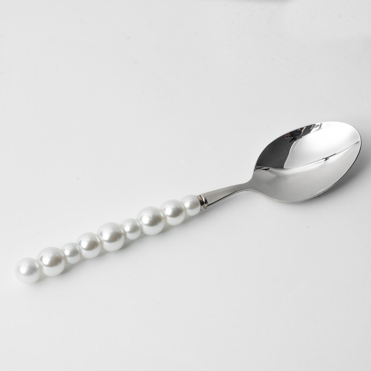 Silver spoon with pearl handle on a light gray background