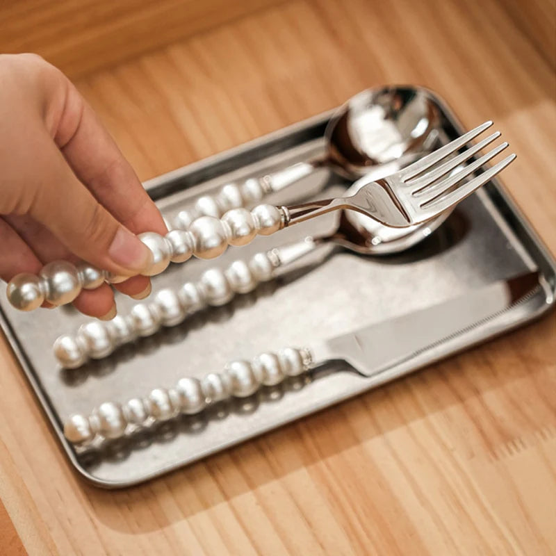 Silver cutlery set with pearl handle design on a tray, held by a hand.