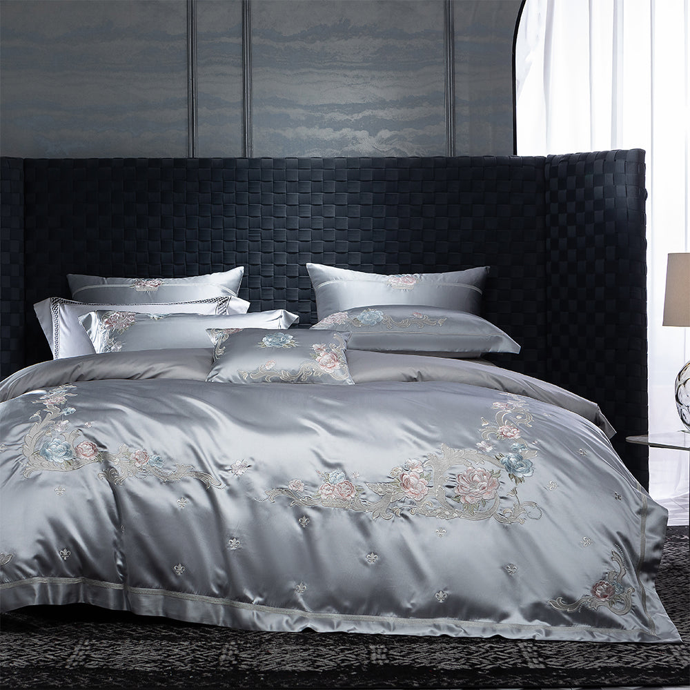 Gray satin bedding set with floral embroidery on a bed in a bedroom.
