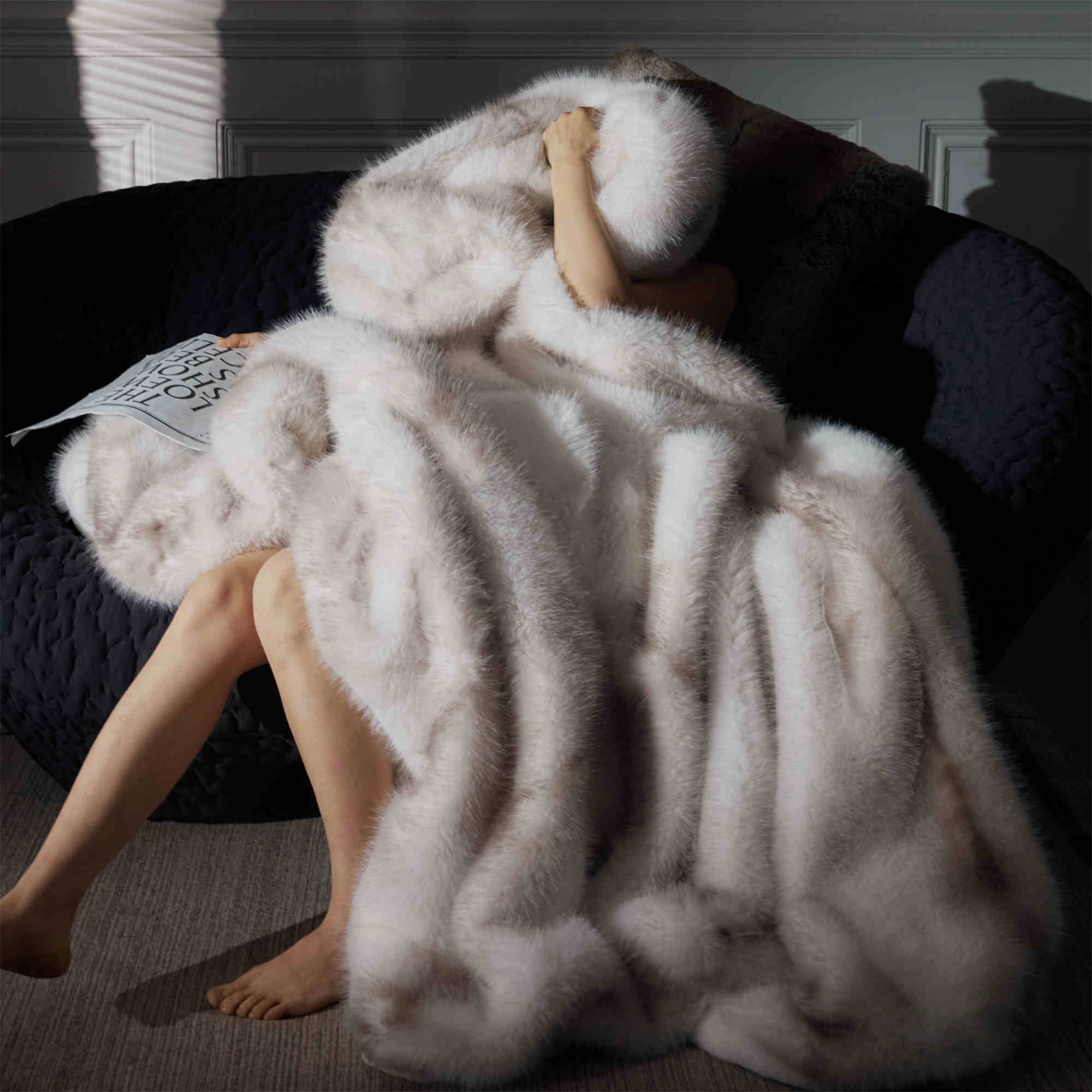 Person wrapped in a fluffy white faux fur blanket on a dark couch.