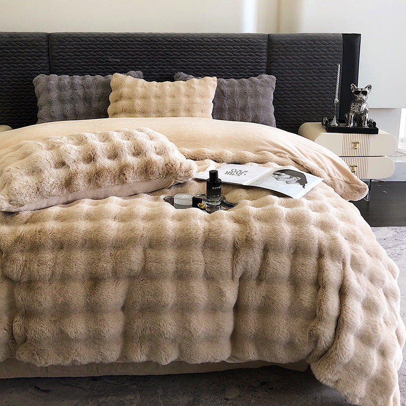Beige fur throw blanket on a bed with pillows and a nightstand.