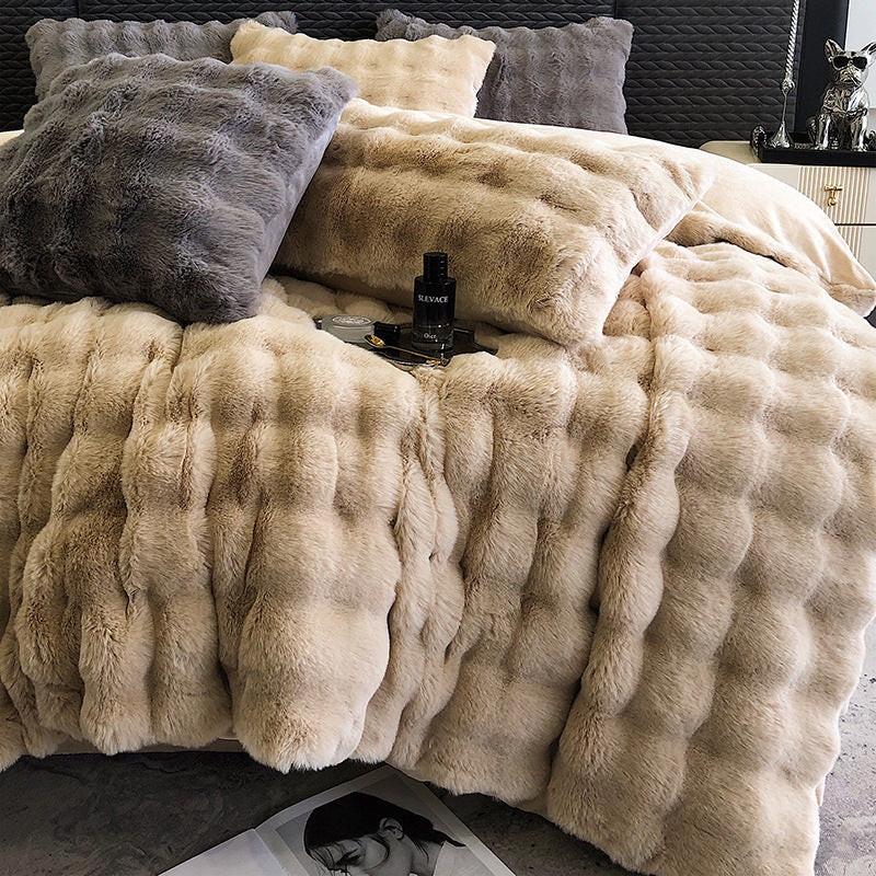 Beige faux fur blanket draped over a bed with decorative pillows.