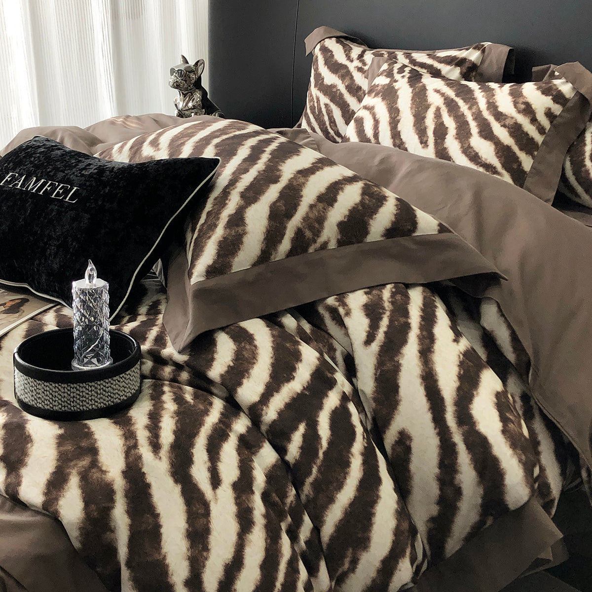 Zebra print comforter with brown accents on a bed, featuring a decorative pillow and small lamp.