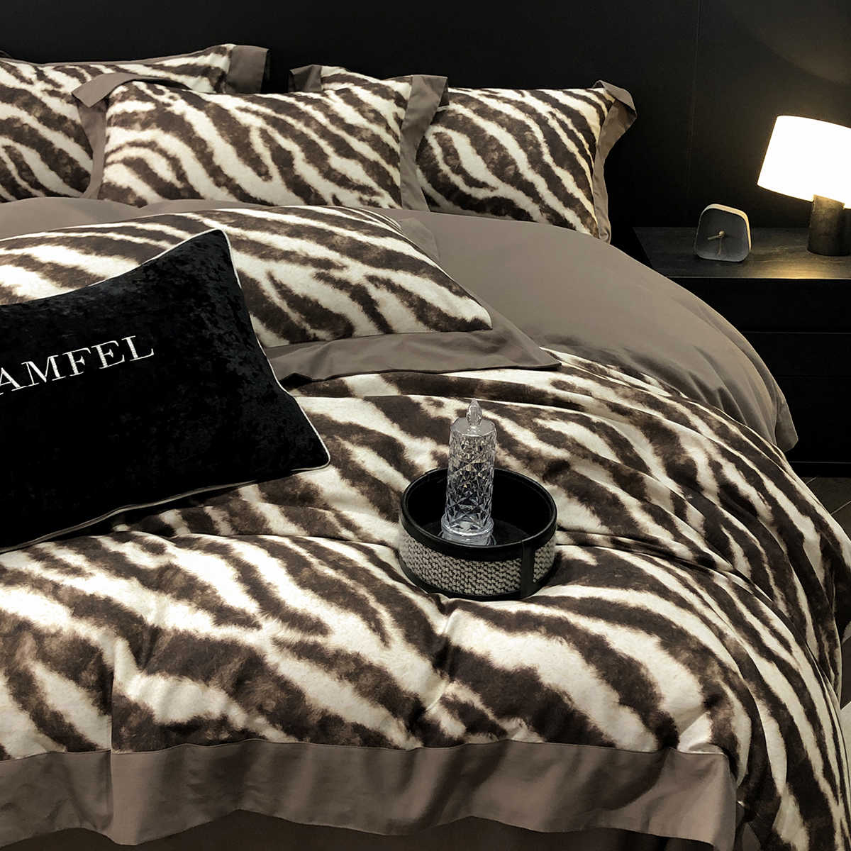 Bed with zebra print bedding and a nightstand with a bottle and lamp.