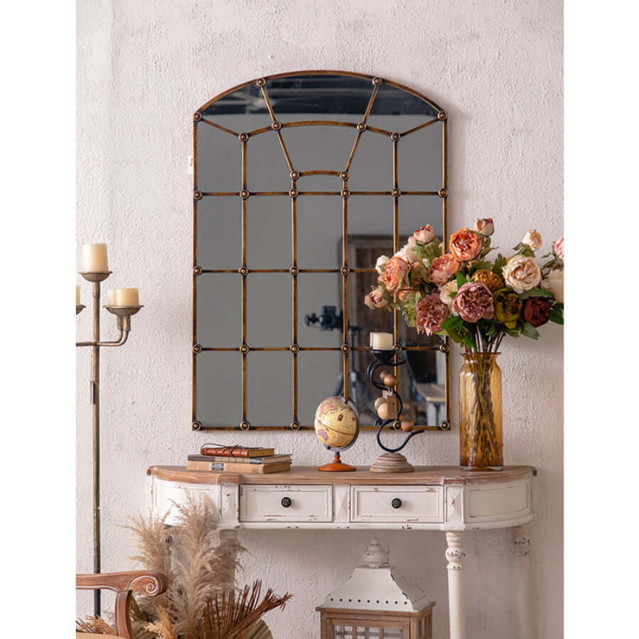 Decorative window pane mirror on a wall above a wooden console table with a vase of flowers.