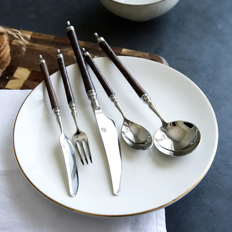 Silver cutlery set with wooden handles on a white plate.