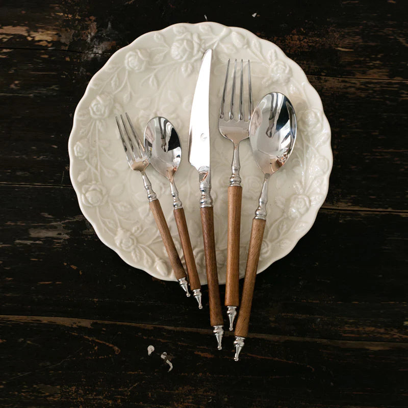Set of silver cutlery with wooden handles on a decorative white plate against a dark wooden background