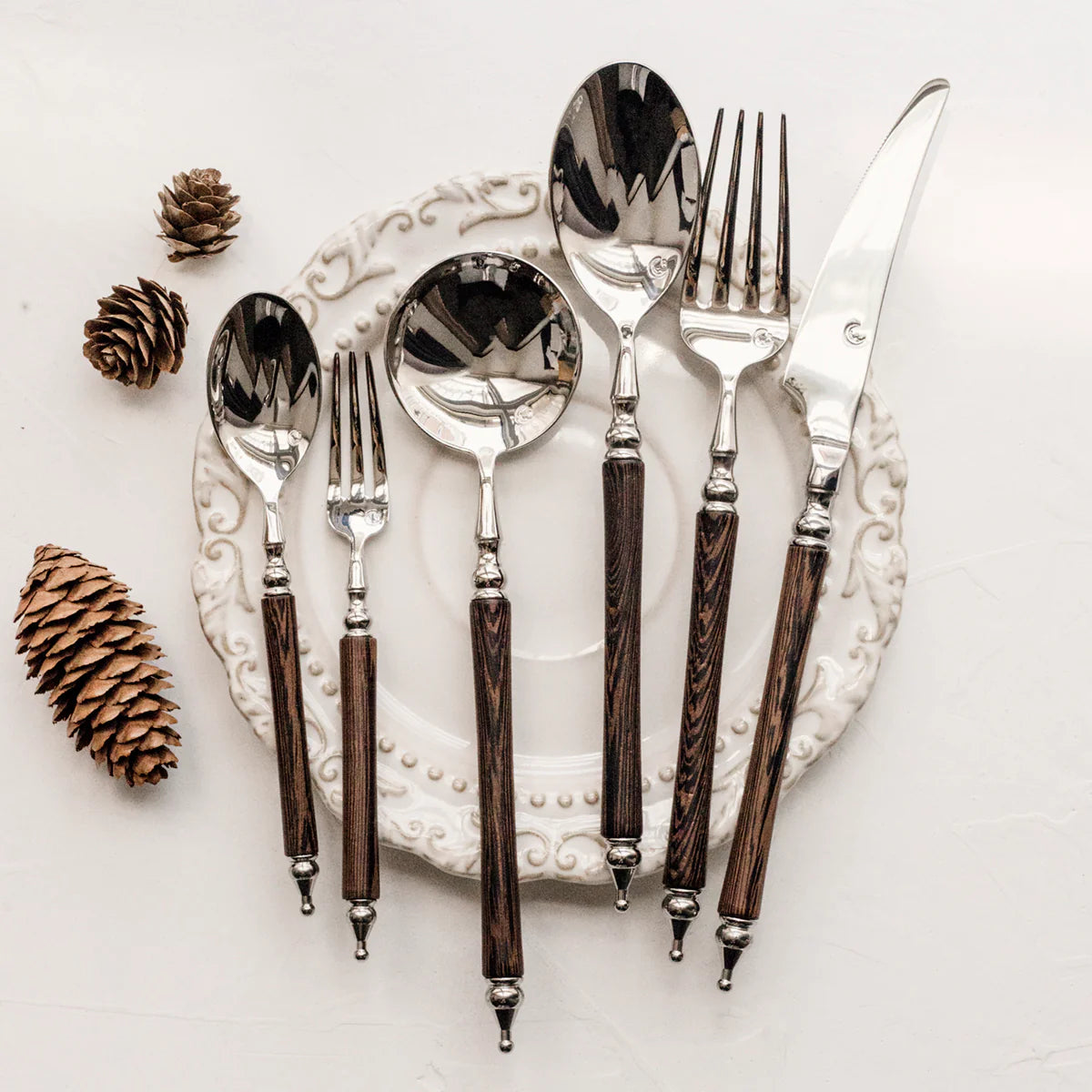Set of silverware with wooden handles on a decorative plate with pine cones.
