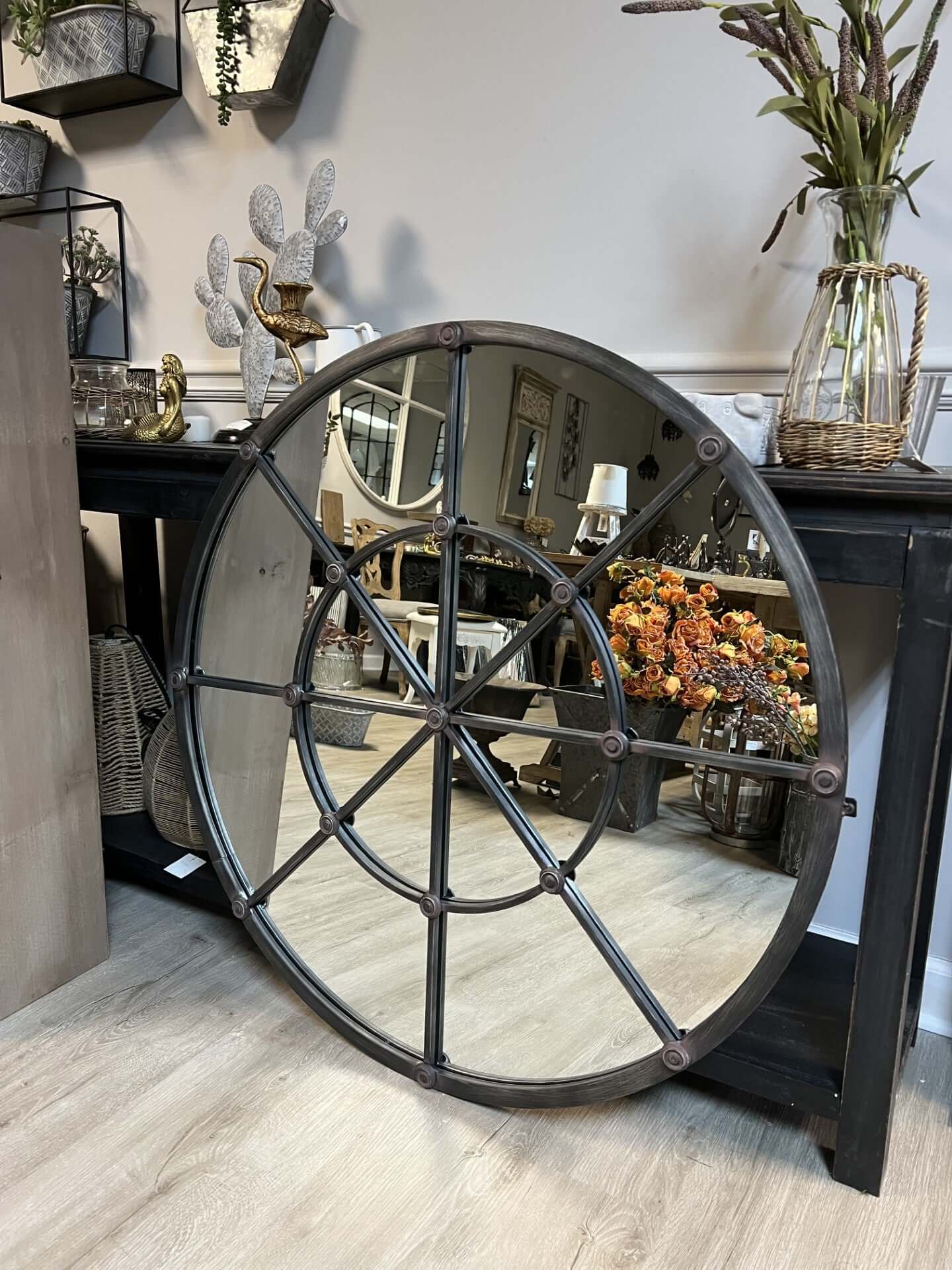 Large round metal mirror with decorative spokes in a room setting.