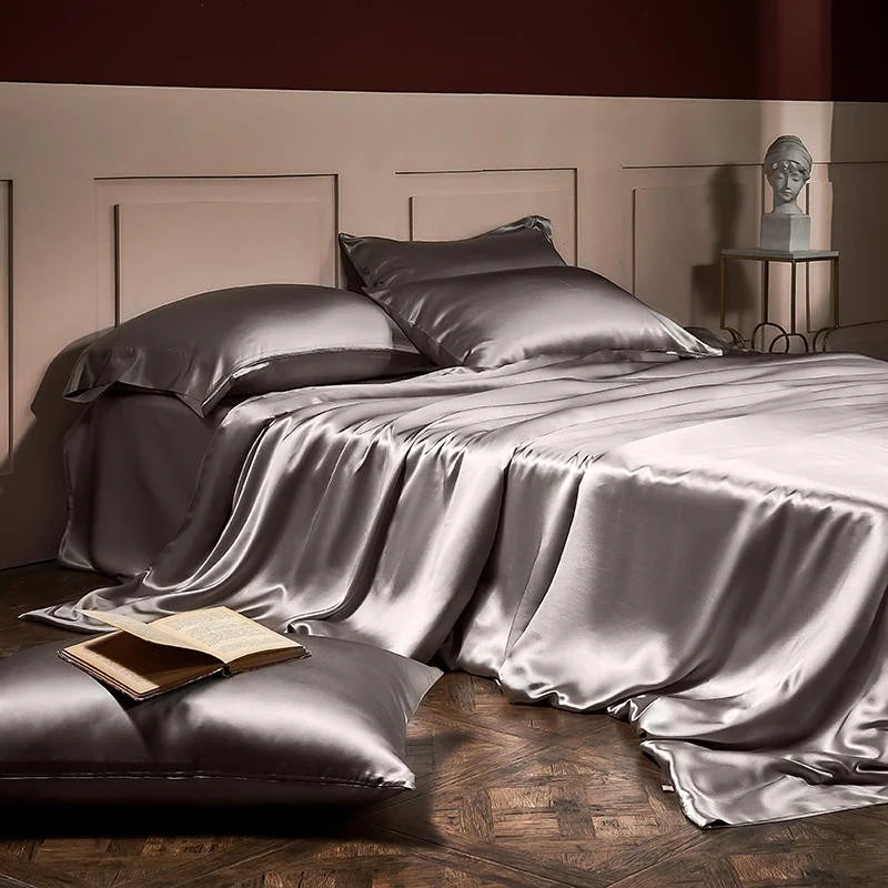 Silver satin bedding set on a bed with an open book and decorative item in the background.