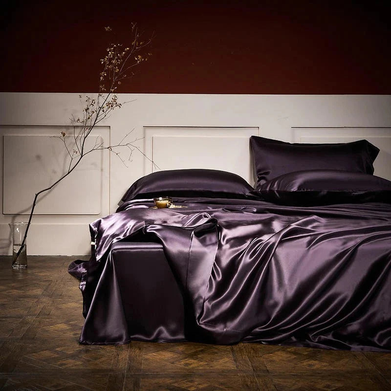 Purple satin bedding set on a bed in a dimly lit room.