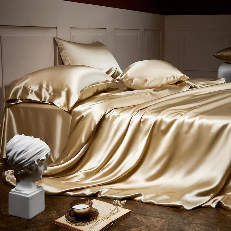 Gold satin bedding set on a bed with decorative items on a wooden floor.
