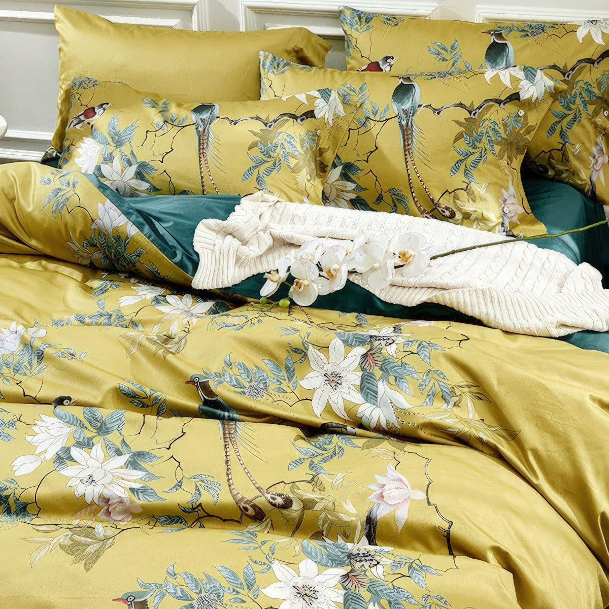 Yellow floral and bird patterned bedding set with white flowers on a bed.