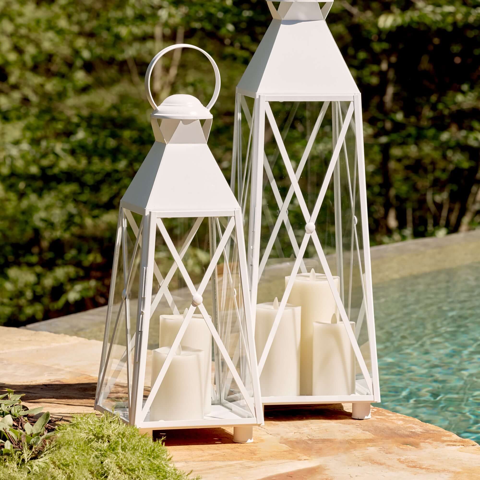 White X framed lanterns with candles on a wooden deck by a pool