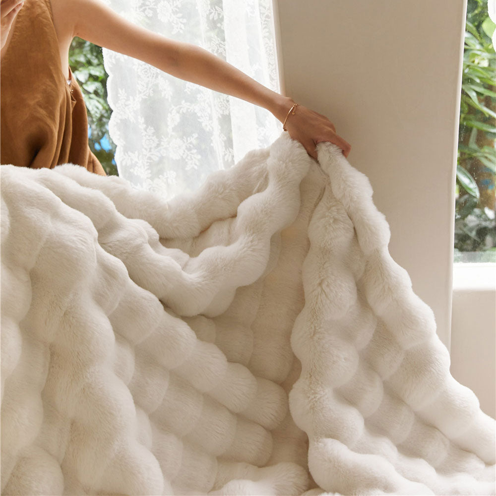 Person holding a fluffy white blanket with a blurred indoor background