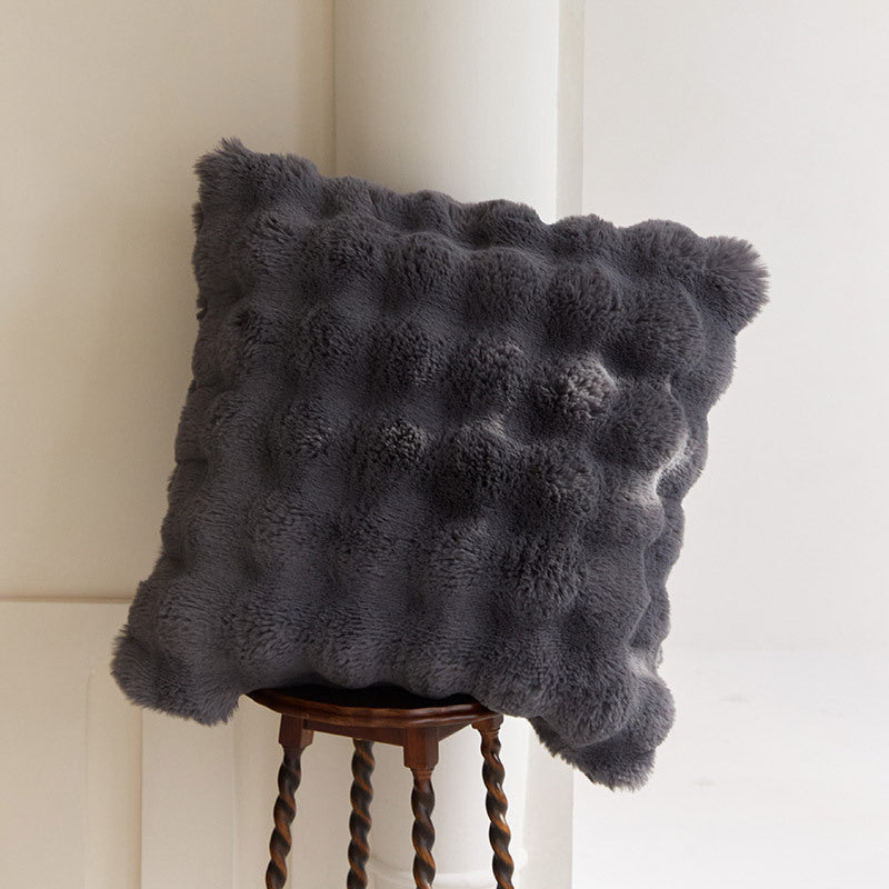 Gray textured pillow on a wooden stool against a neutral wall