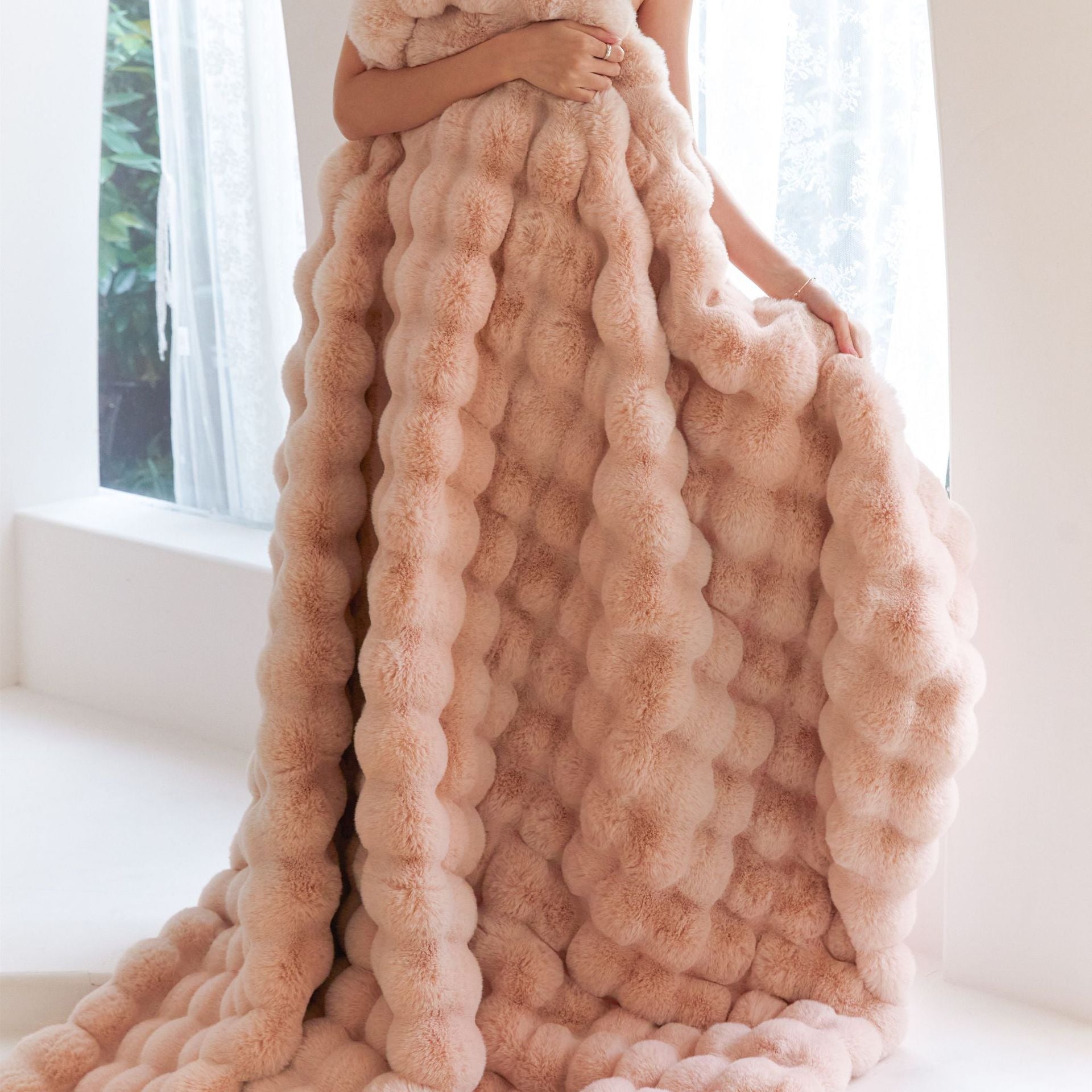 Person holding a large, textured pink blanket in front of a window.