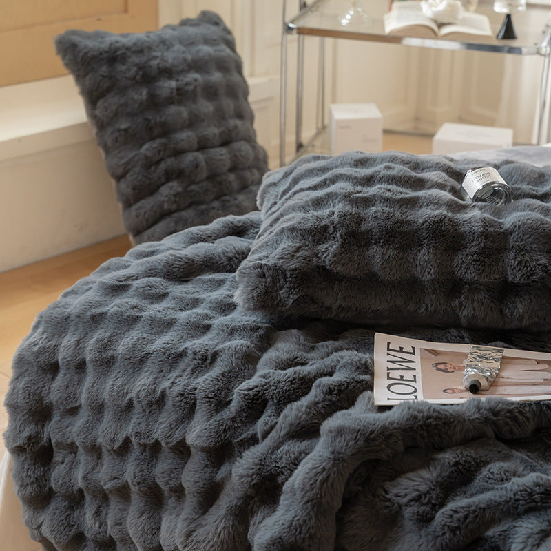 Gray textured blanket and pillow on a surface with a magazine underneath.