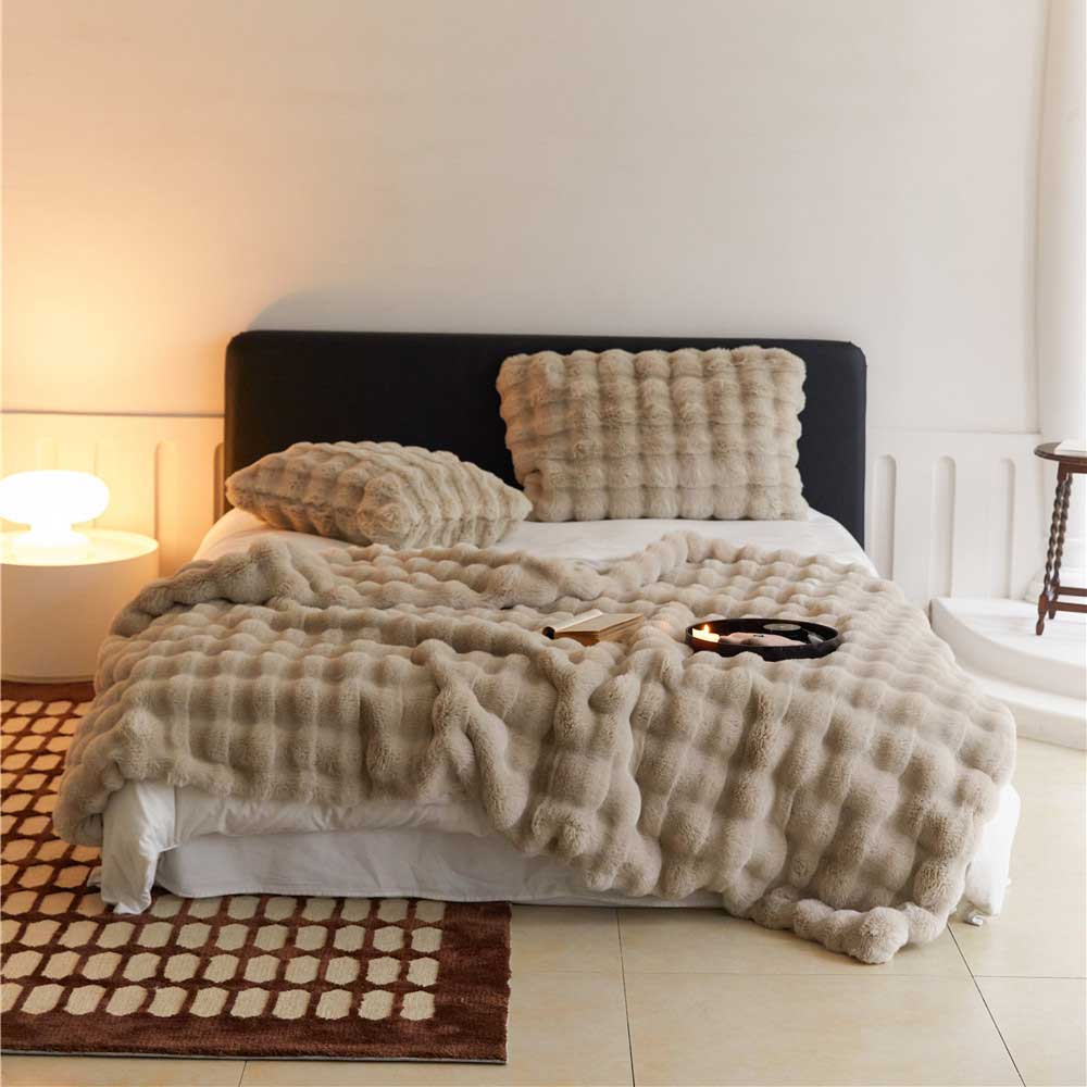 Beige textured blanket and pillows on a bed in a bedroom setting.