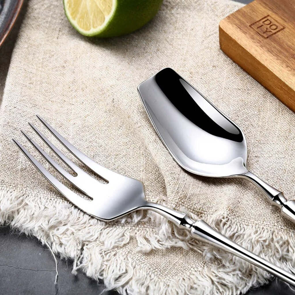 Stainless steel fork and spoon on a textured surface with a lime and wooden block in the background.