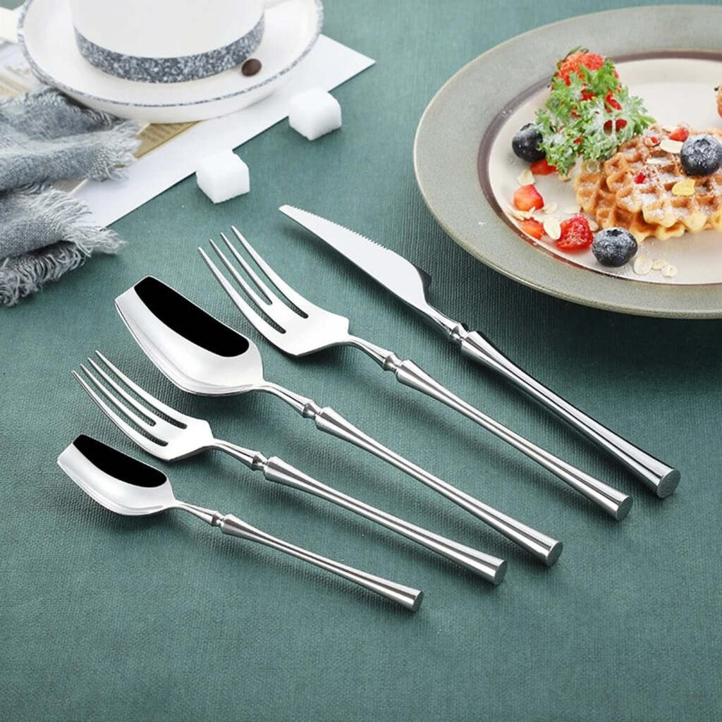 Set of silver cutlery on a green tablecloth with a plate of waffles and berries in the background.