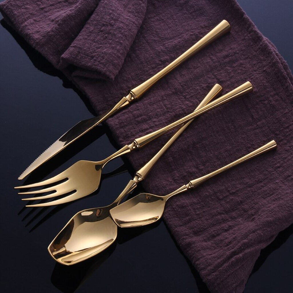 Set of gold cutlery on a dark surface with a purple cloth