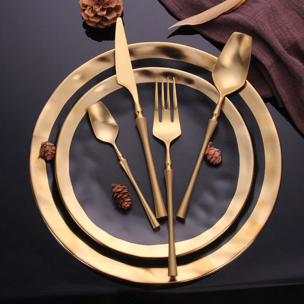Gold cutlery set on a dark surface with pine cones