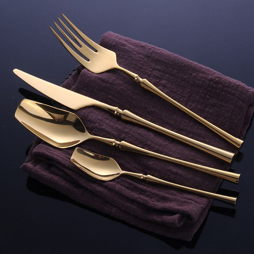 Set of gold cutlery on a purple cloth against a dark background