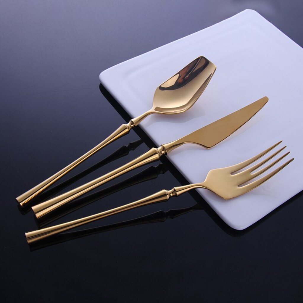 Set of gold cutlery including a spoon, knife, and fork on a white square plate against a dark background.