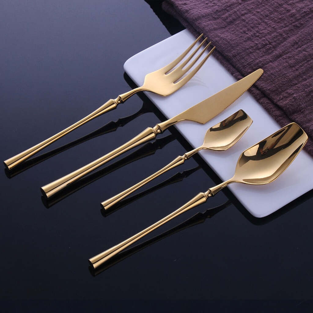 Set of gold cutlery including a fork, knife, and two spoons on a dark surface.