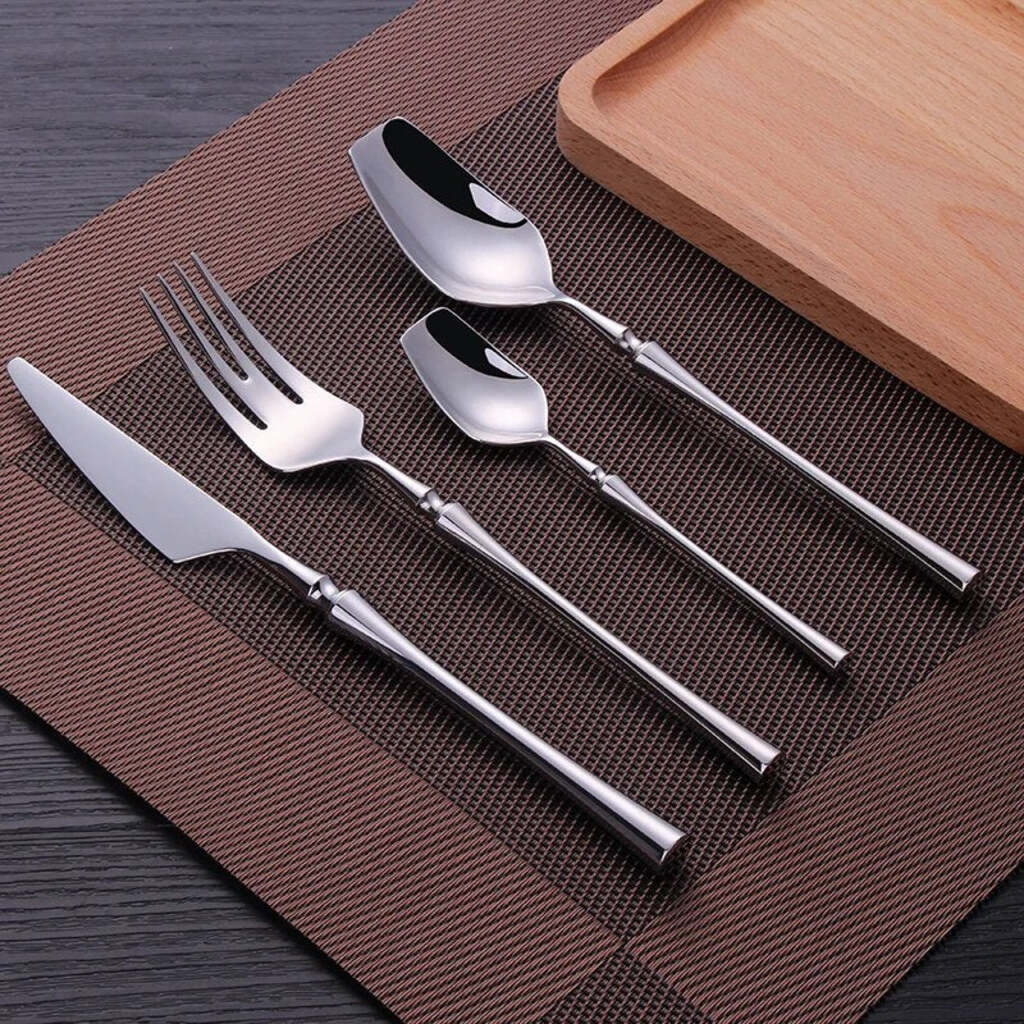 Set of silver cutlery including knife, fork, and spoons on a brown mat with a wooden tray.
