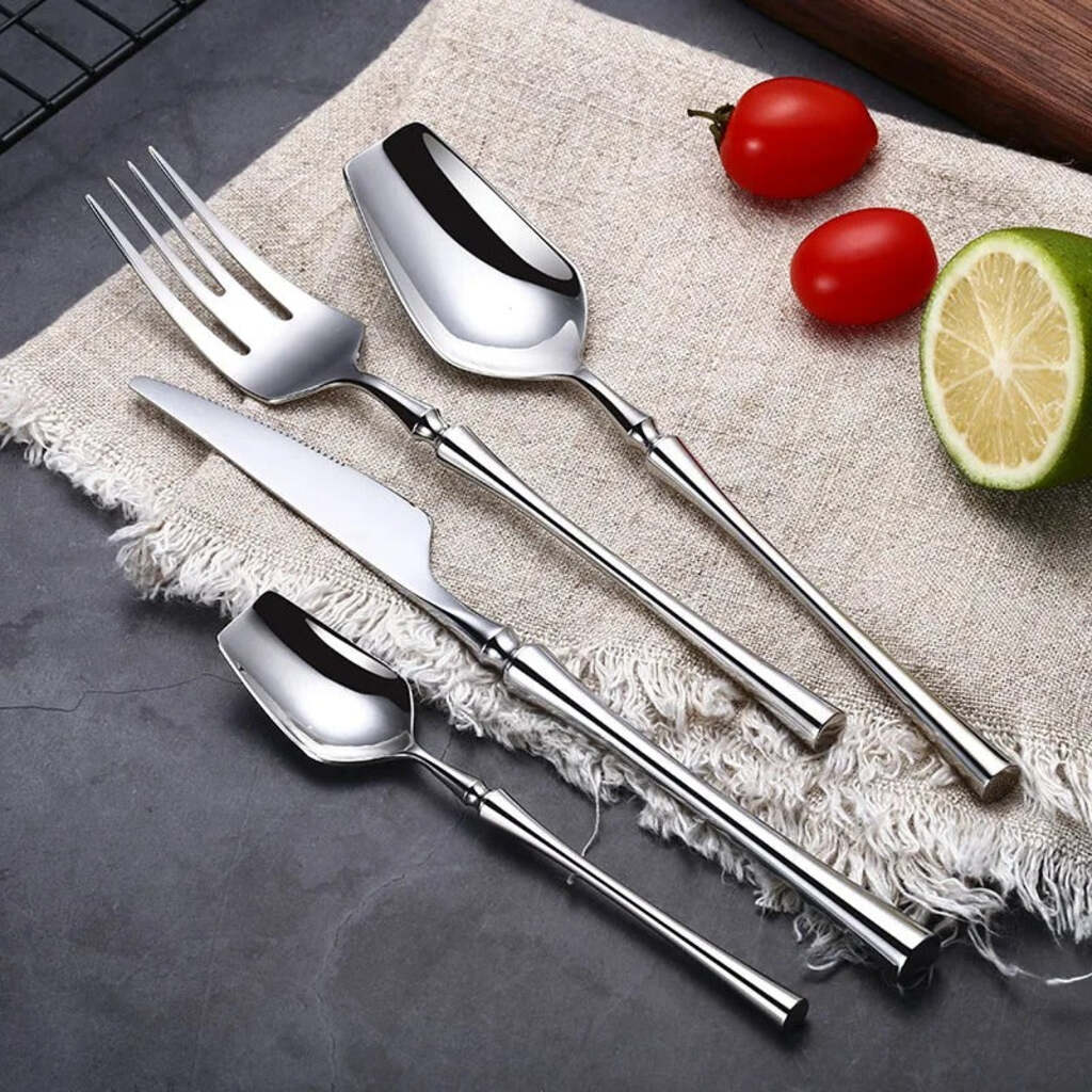 Set of silver cutlery on a textured surface with tomatoes and a lime.