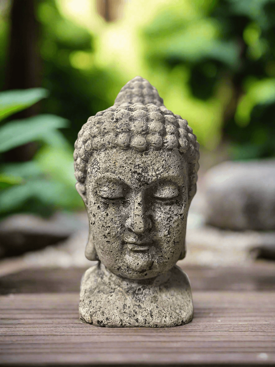 Stone Buddha head sculpture on a wooden surface with a blurred natural background