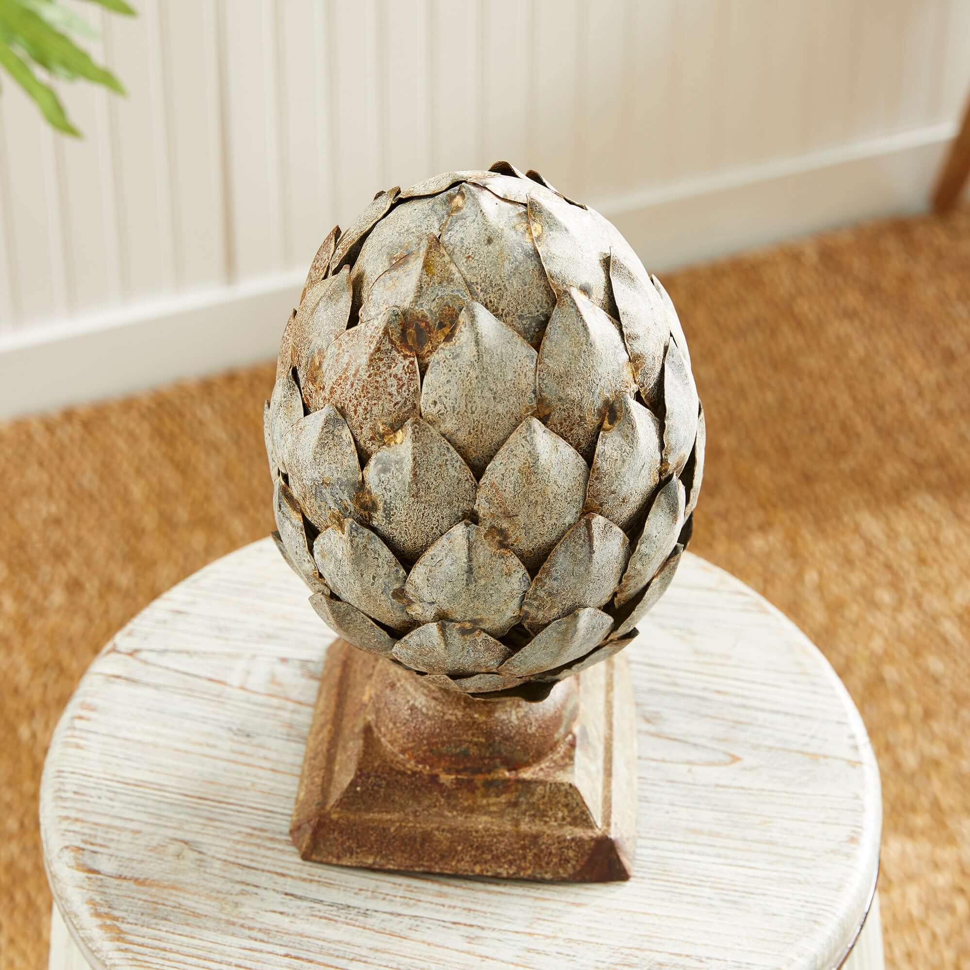 Decorative artichoke sculpture on a wooden pedestal against a neutral background