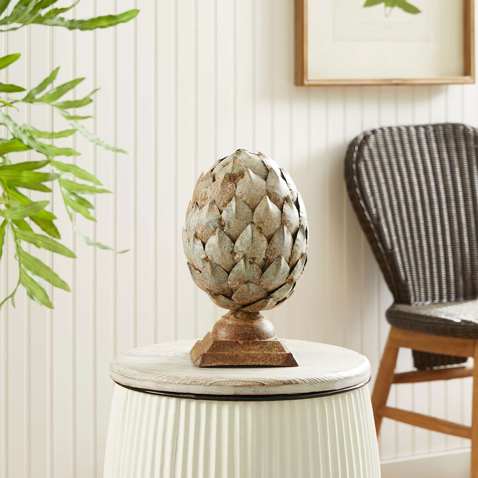 Decorative artichoke sculpture on a small round table with a chair and plant in the background