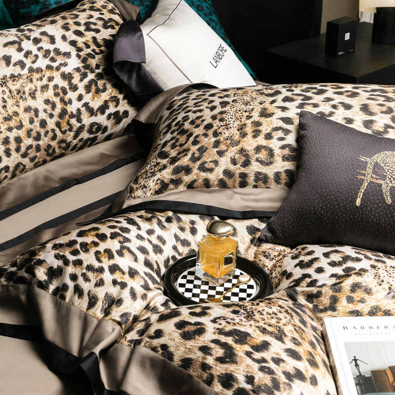 Leopard print pillows and a bottle of perfume on a checkered coaster on a bed.