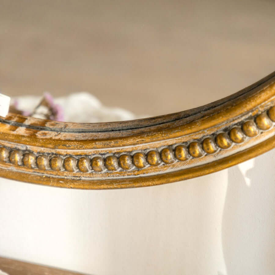 Close-up of a Gilded wood frame mirror with classic beaded (pearl) molding on a white surface.