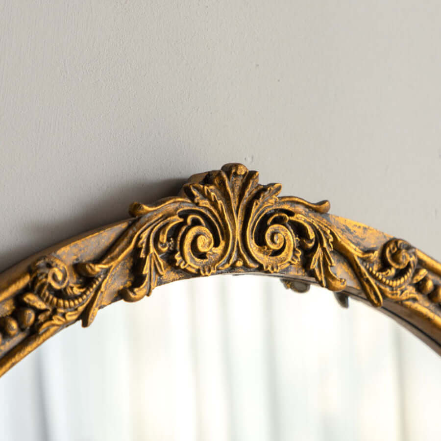 Close up of carved acanthus scroll cresting on decorative gold mirror frame on a plain background