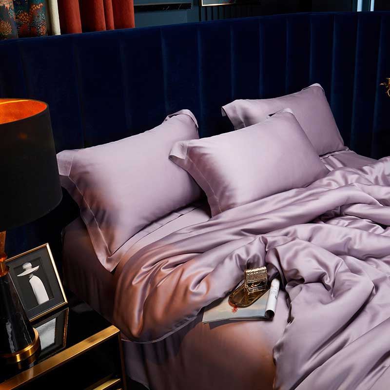 Purple bedding set on a bed with a lamp and decorative items in the background.